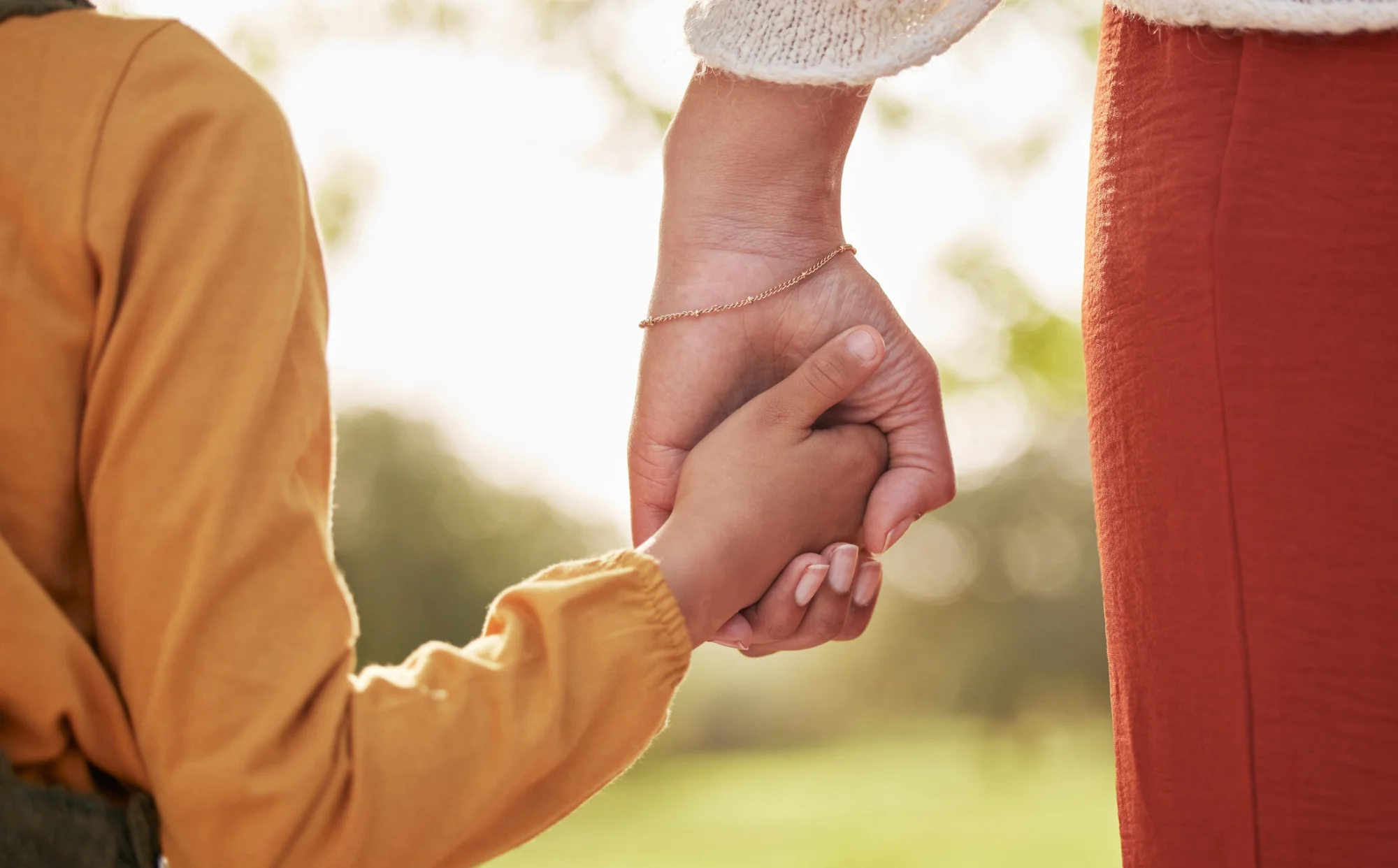 A mother holding hands with her kid walking in park