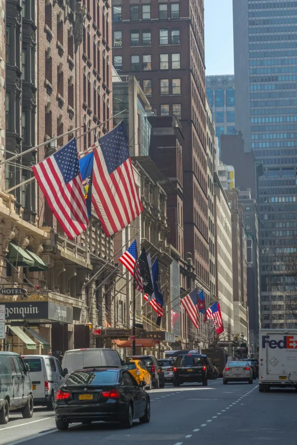 A busy street in New York City lined with American flags and traffic.