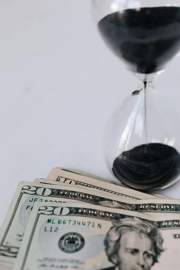 An hourglass next to U.S. dollar bills, symbolizing time and money.