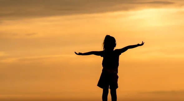 Silhouette of a little girl with hands raised in the sunset 