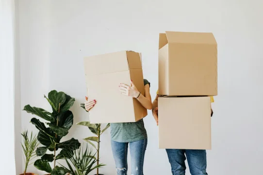 Two people holding cardboard boxes, likely moving into a new home.