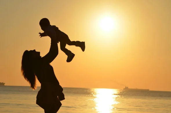 A mother lifting her child at sunset by the sea.