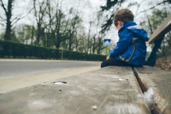 A child sitting alone on a wooden bench