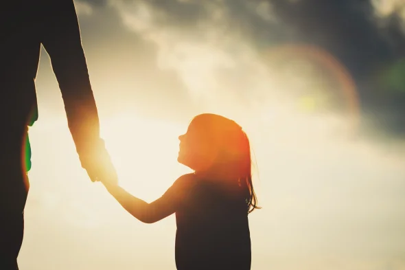 Silhouette of little girl holding parent hand at sunset