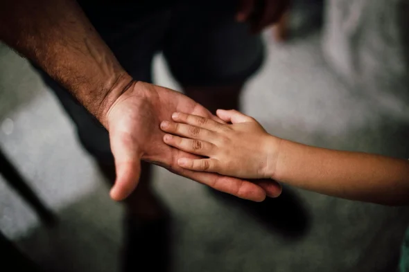 An adult's hand gently holding a child's hand, symbolizing care.