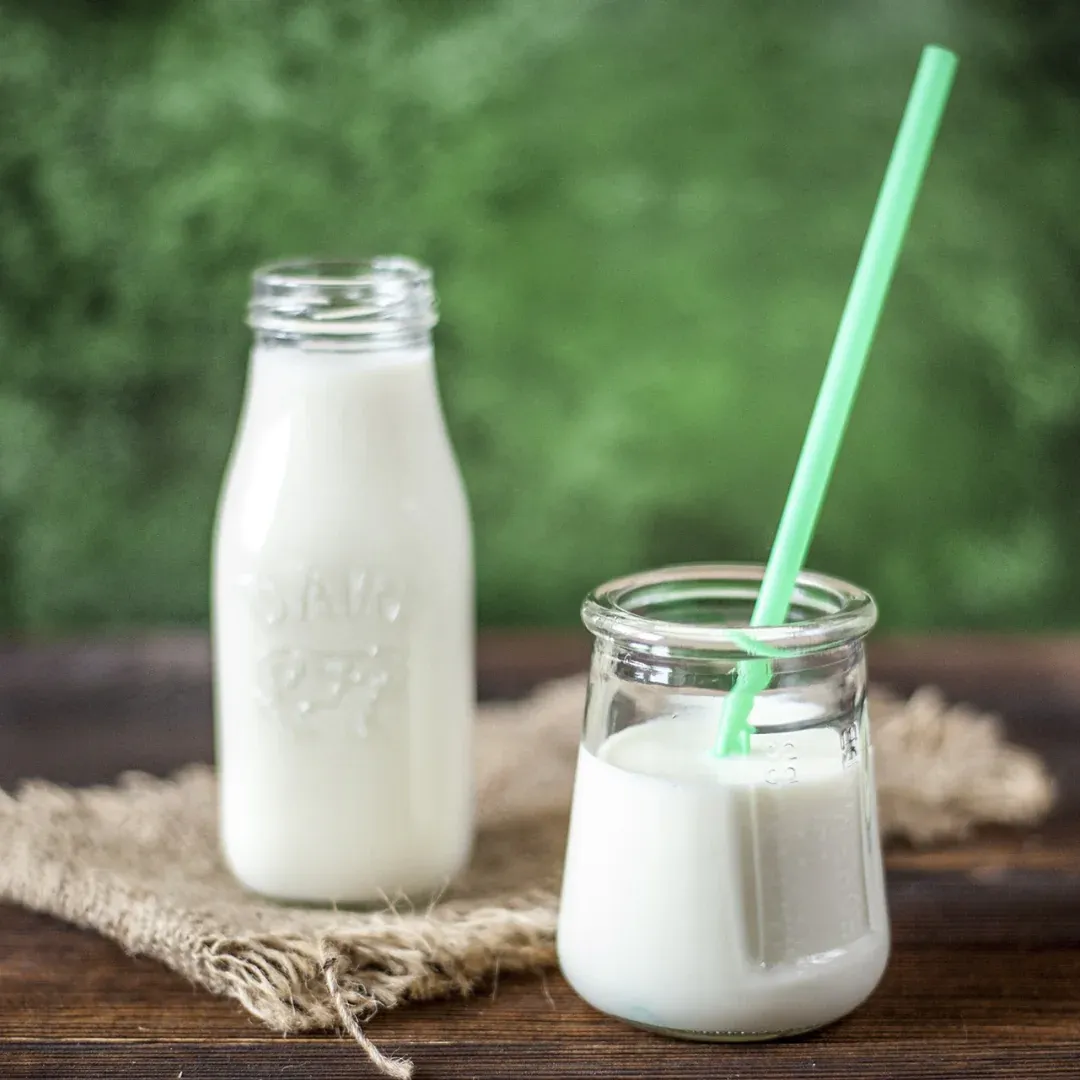 A glass of milk and a pitcher of milk on a table.