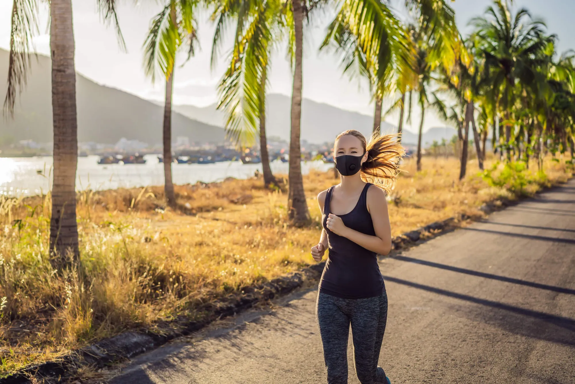 A woman is jogging outdoors and she is wearing a mask.