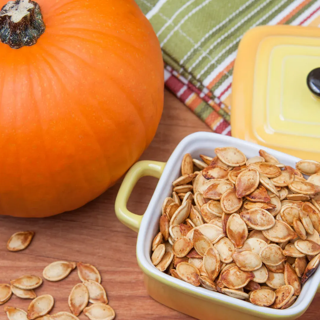 A pumpkin on a table next to a bowl of pumpkin seeds.