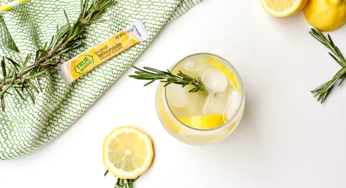 A glass of rosemary lemonade alongside a True Lemon Original Lemonade packet.