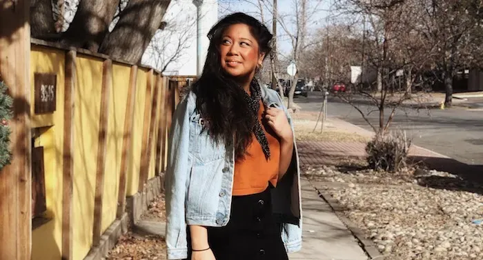 Rachel is standing on a sidewalk. She is looking off to the distance.