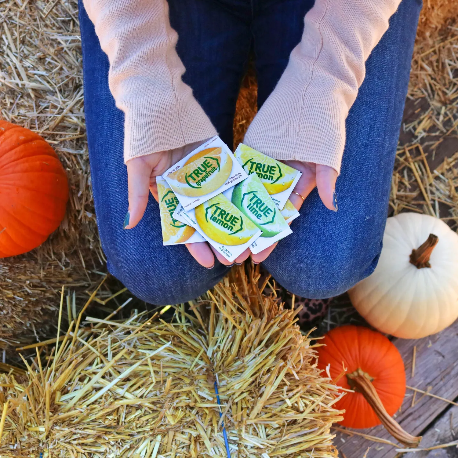 A woman kneeling in some hay holding True Lemon and True Lime packets in her hand.