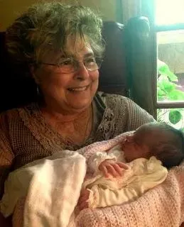 Teresa is sitting down smiling and holding a baby.