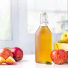 A bottle of apple cider vinegar next to some apples.