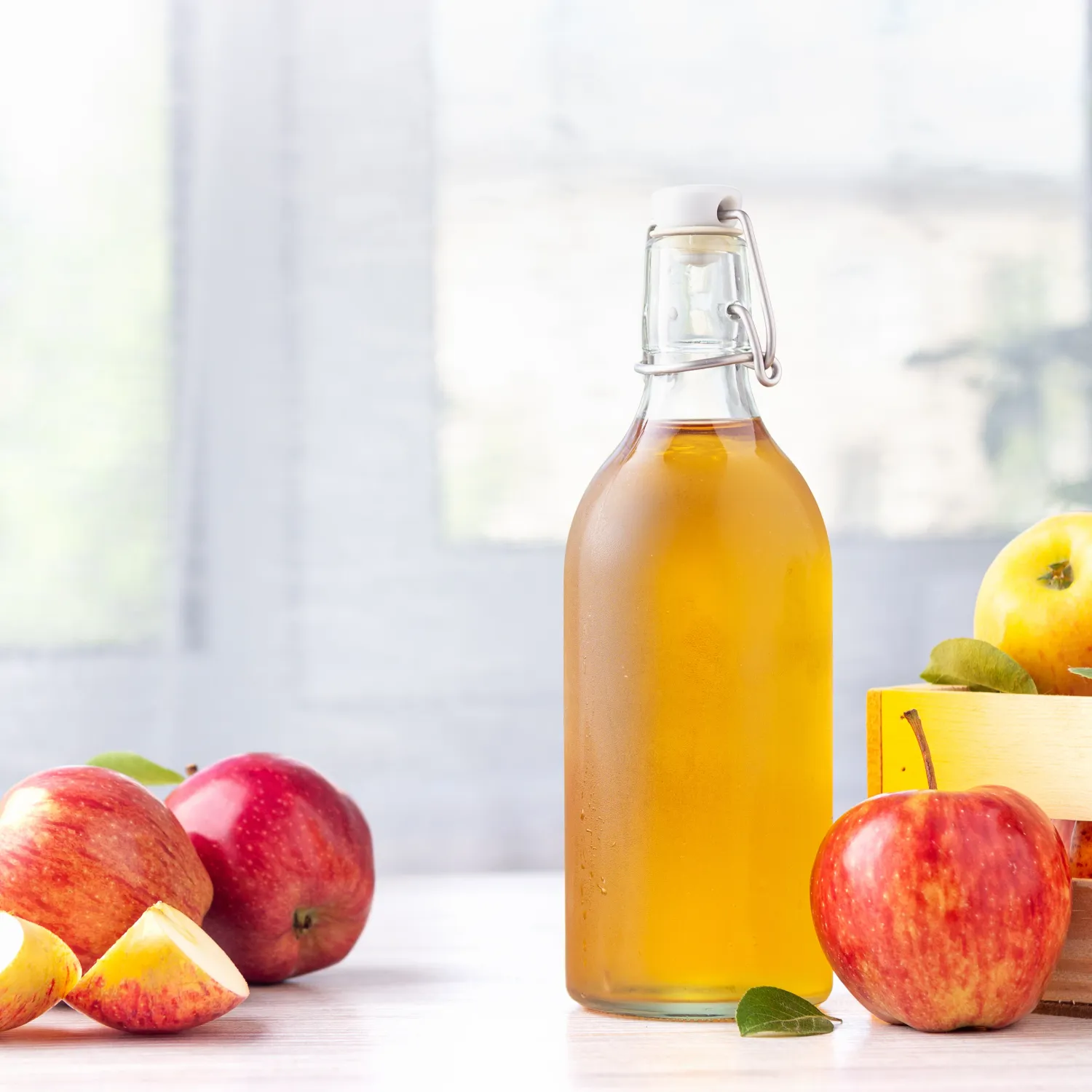 A bottle of apple cider vinegar next to some apples.
