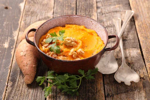 Delicious mashed sweet potatoes topped with a hint of ginger, served in a white bowl, showcasing a bright and creamy dish with a rich orange color.