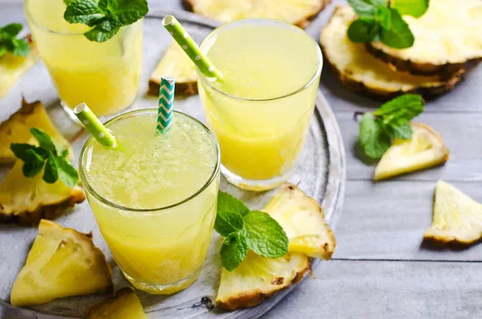 A tray of 3 glasses of True Lime Pineapple Mint Punch. There are slices of pineapple around it.