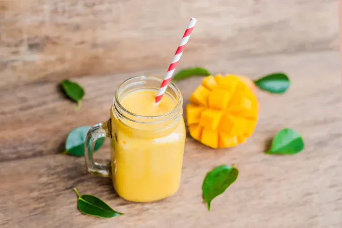 A mango smoothie in a glass on a table with a sliced mango behind it.