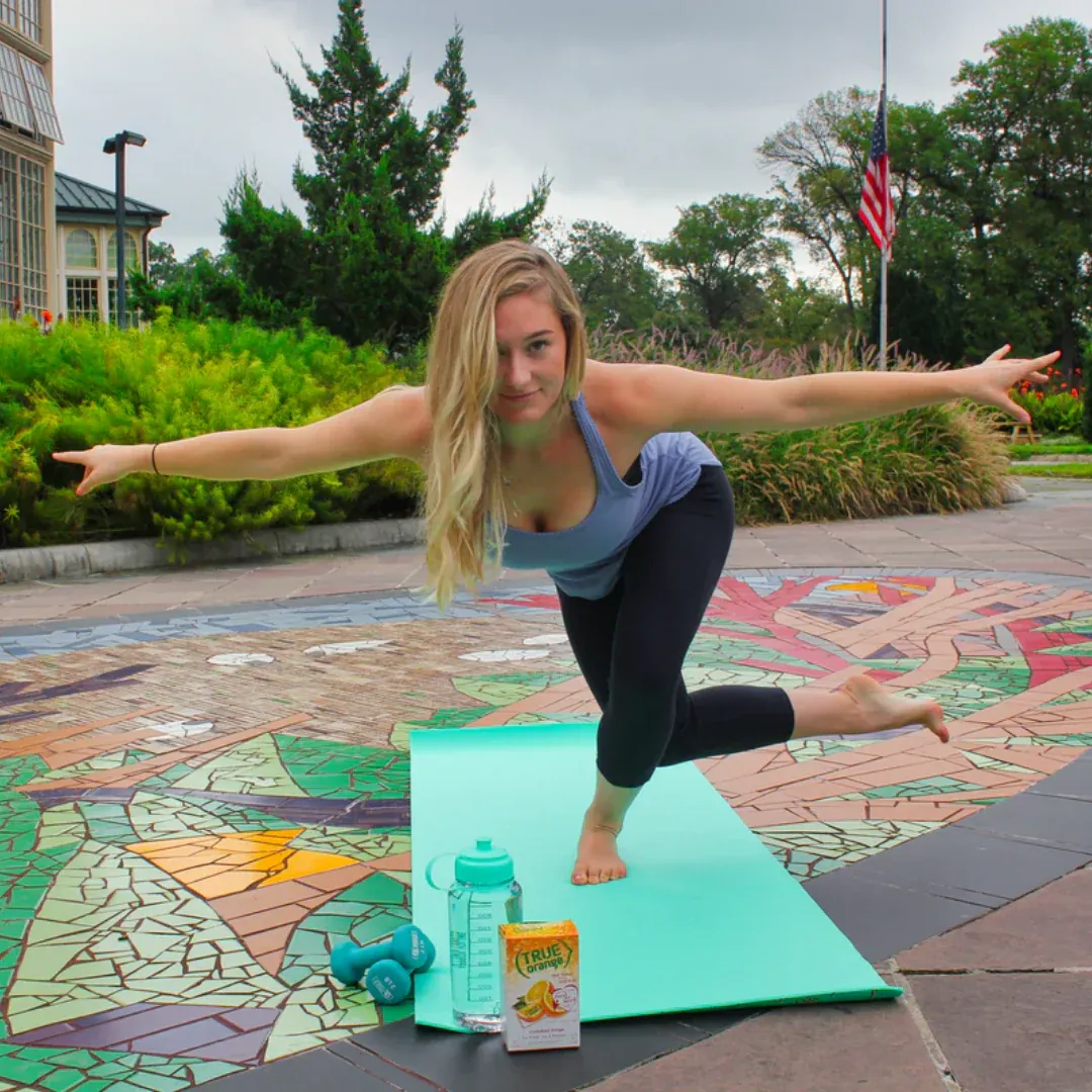 A woman doing yoga outside. There is box of True Orange next to her.