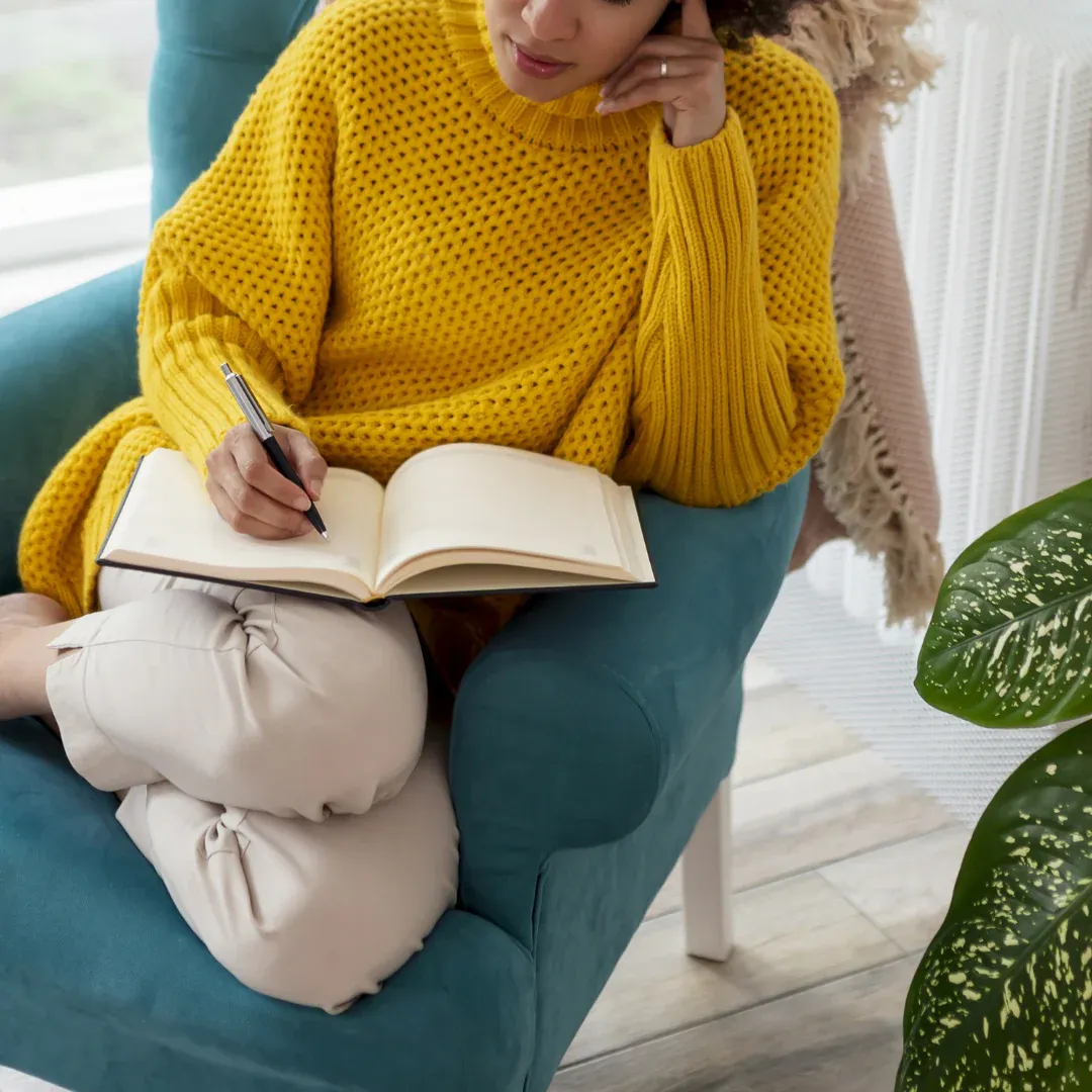 A woman sitting in a chair writing in a journal.