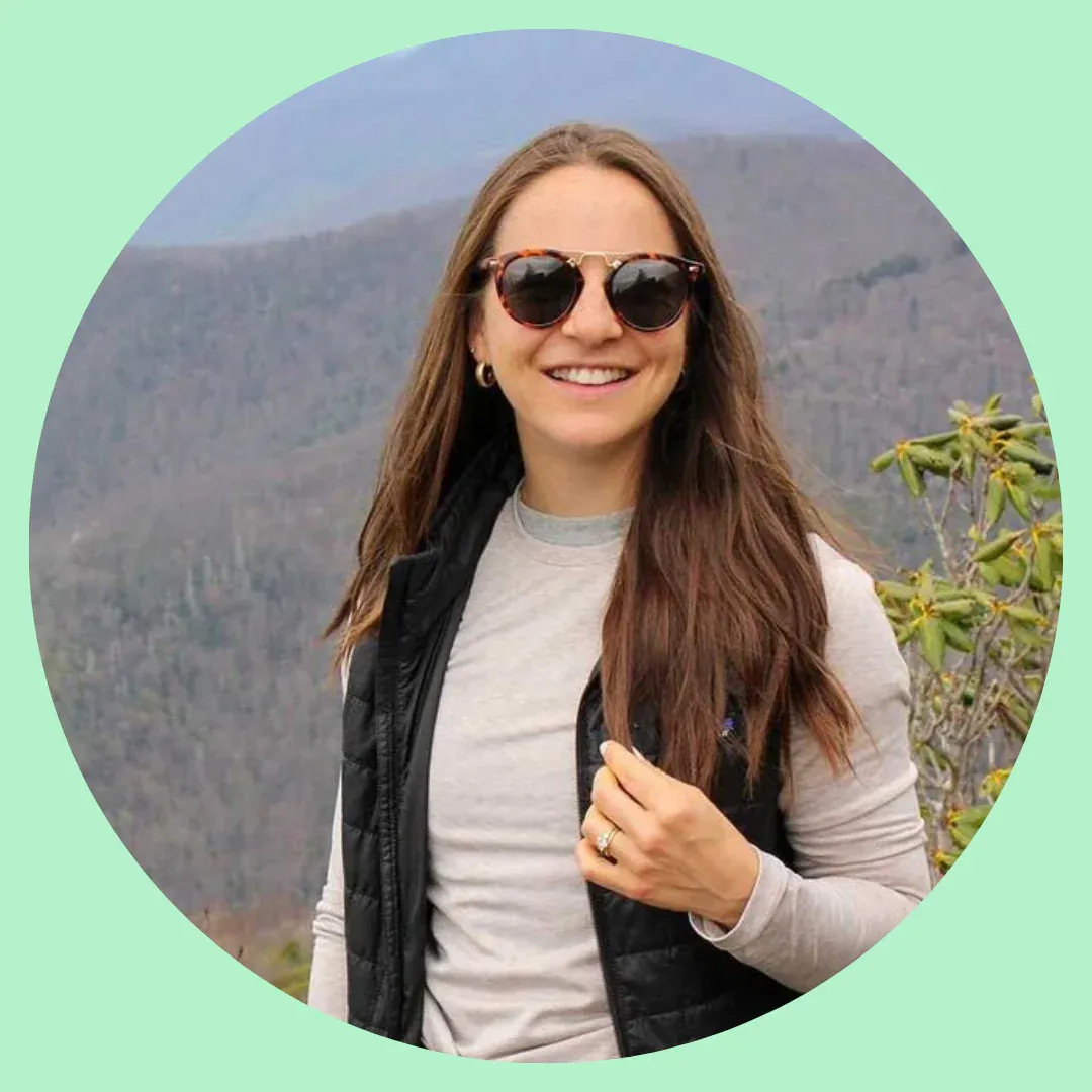 A photo of Clara Norfleet. She is smiling and standing in front of a mountain scenery.