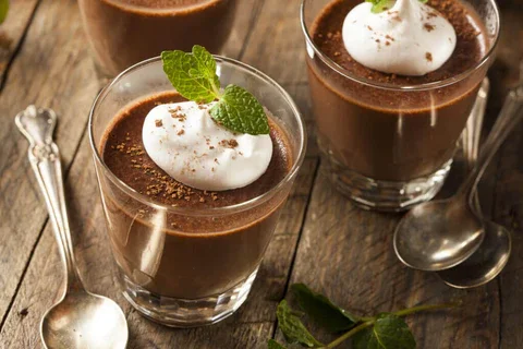 Rich chocolate mousse topped with a twist of orange zest, served in a clear glass dish, combining smooth, decadent chocolate with a bright mint garnish.