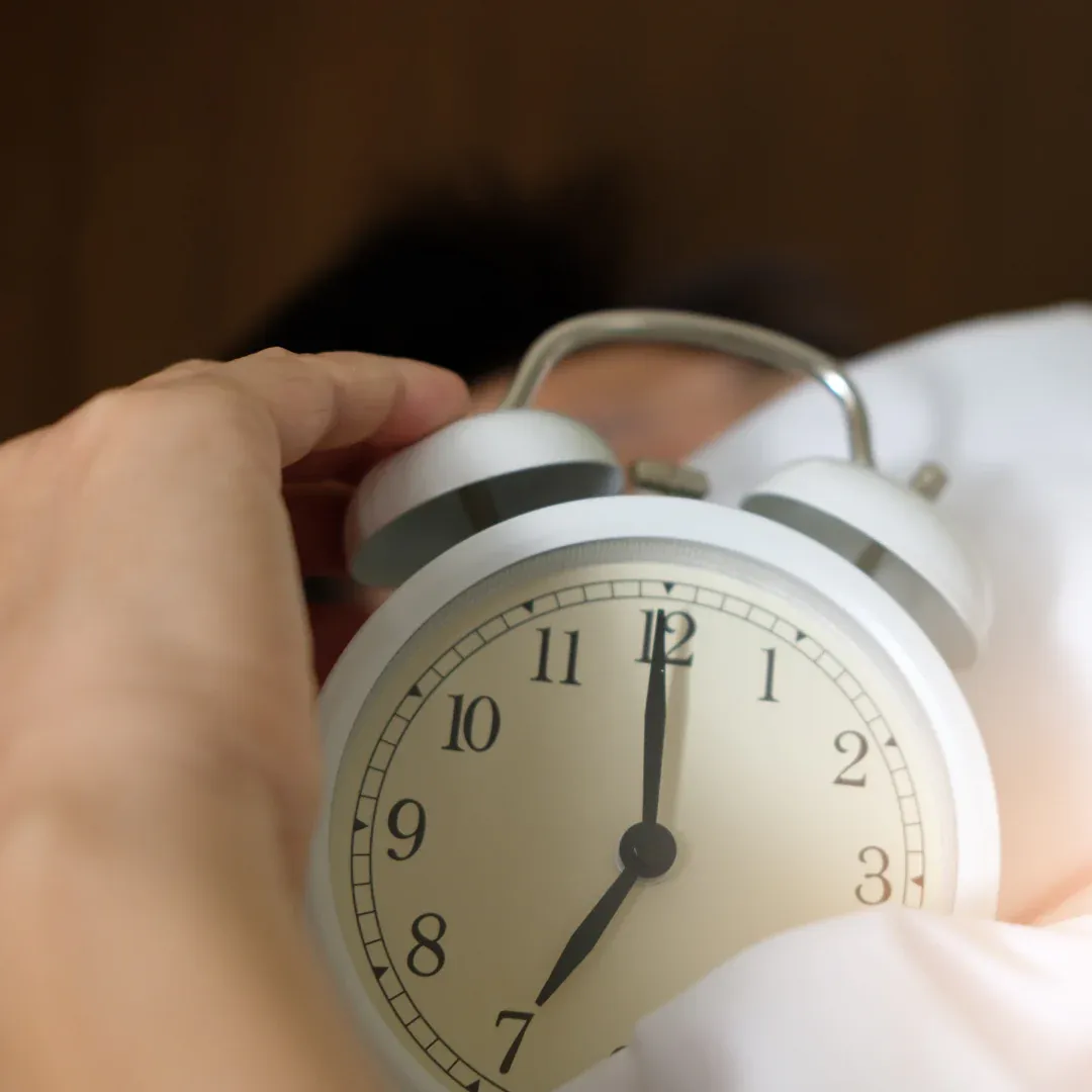 A person who is alseep holding an alarm clock.