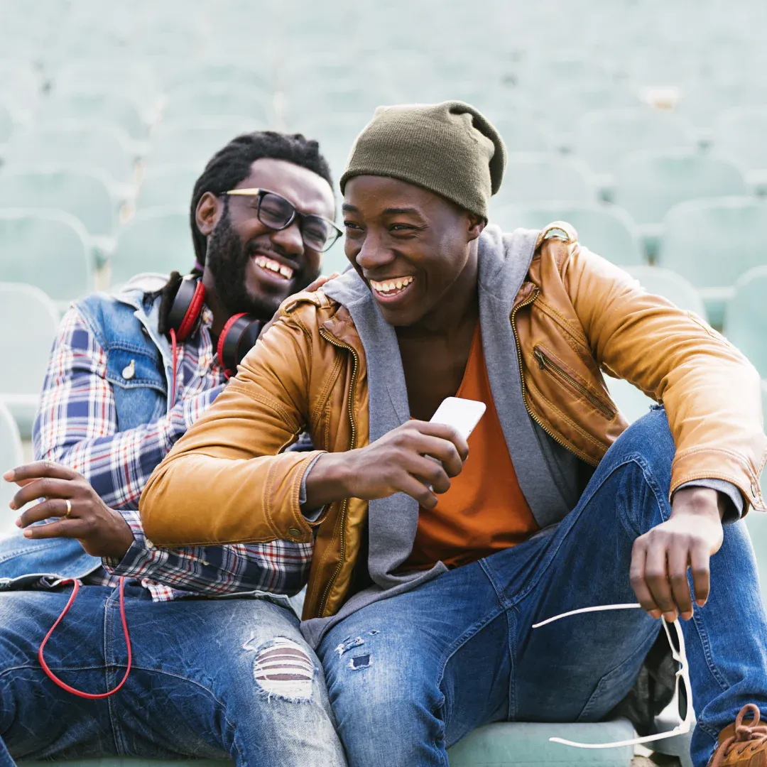 Two men sitting in a stadium laughing.
