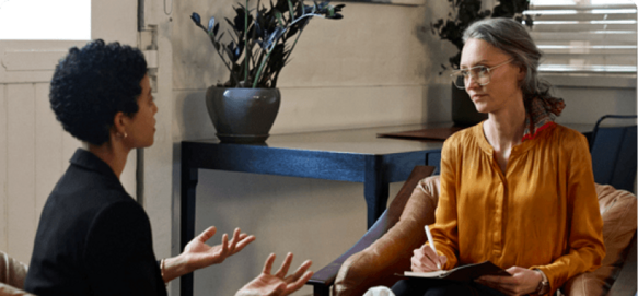 Therapist taking notes while listening attentively to a patient during a therapy session
