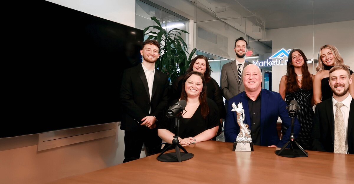 Eight professional team members posing in a MarketCrest office, with microphones and an award visible on the table.