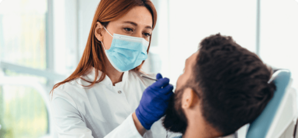 Dentist wearing a face mask and gloves examining a patient's teeth in a clinic