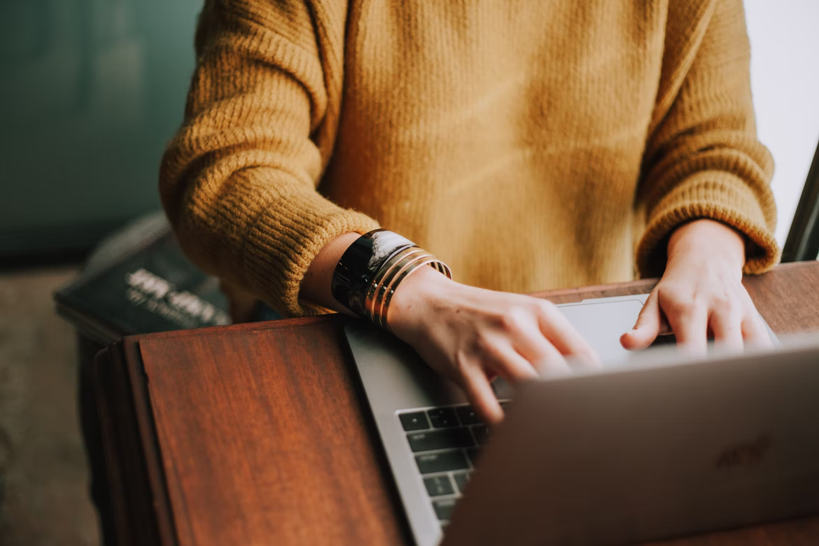 Person in yellow sweater typing on Apple laptop