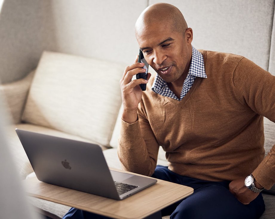 man talking on smartphone while looking at laptop screen