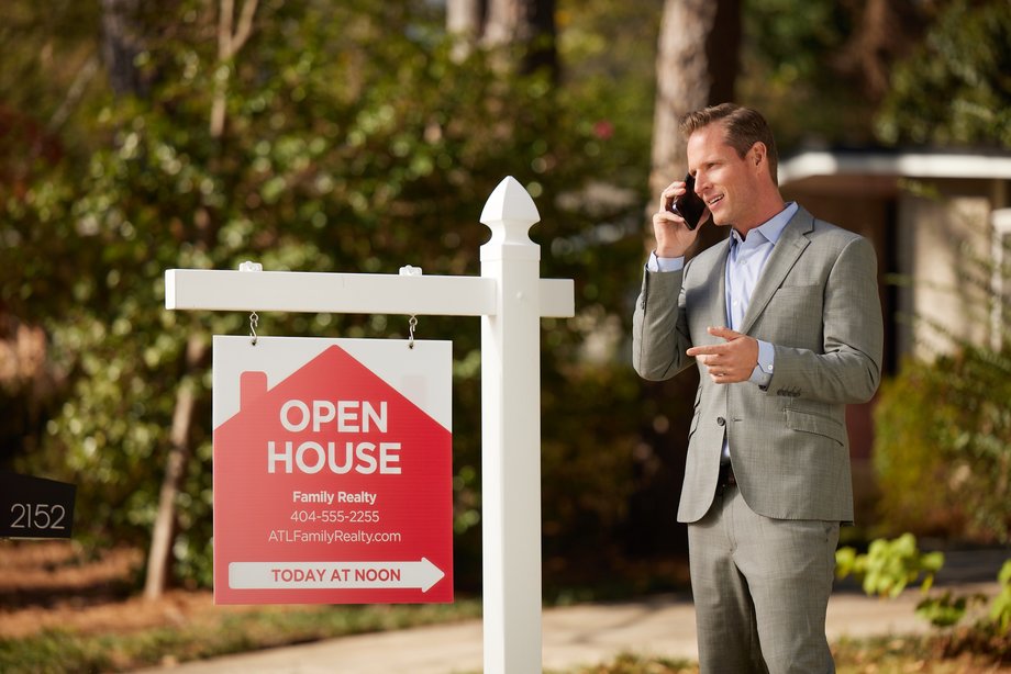 real estate agent standing by open house sign talking on the phone