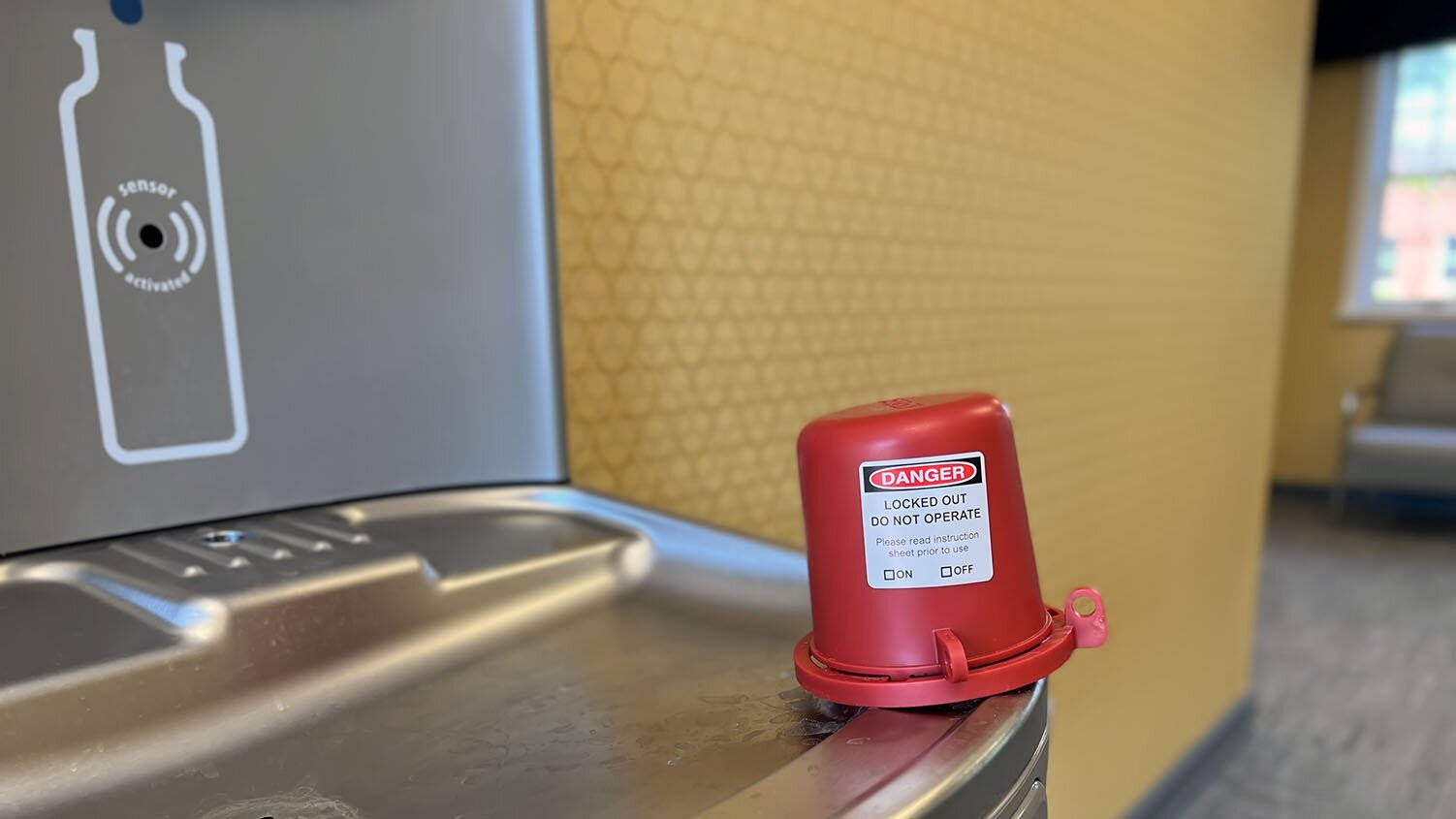 Image of a water filling station with a locked cap that says 'Danger' over the drinking faucet portion of the station.