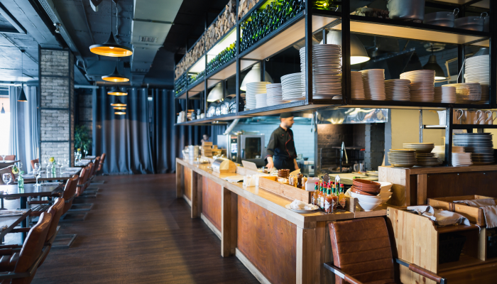 Image of a restaurant with the kitchen open and visible to the main dining area. White plates are stacked on shelves suspended from the ceiling around the kitchen counters.