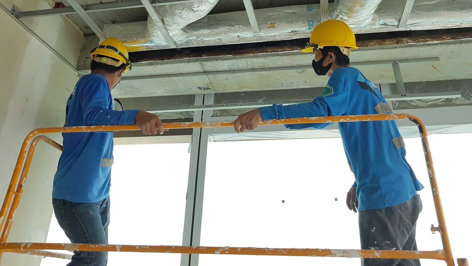 2 workers wearing hard hats and masks are holding on to hand rails in a building under construction.