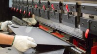 Worker using a press brake machine to bend a sheet metal panel in a manufacturing setting 