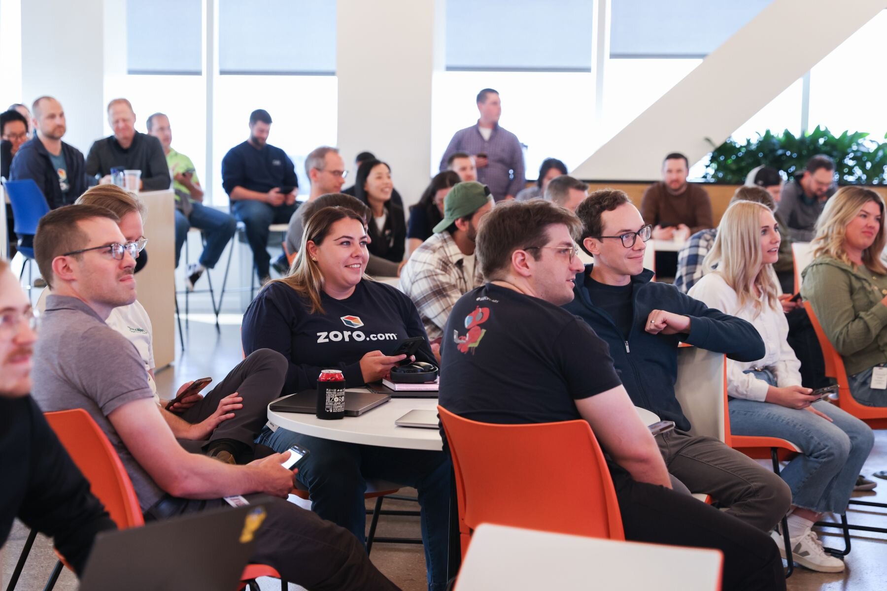 2 zoro staff consulting at a cafe table in sun shinning through windows with high rise buildings in background.