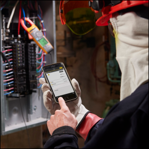 Technician in full PPE using the Fluke Connect app on a cell phone to monitor readings from a safe distance.