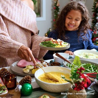 A mother fills her daughter's plate with creamed corn for Christmas dinner.