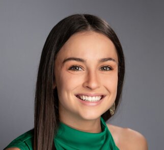 A man wearing a cowboy hat, brown jacket, and jeans is kneeling by a tripod over a small campfire, holding a blue 4Patriots food pouch in his hands. A black pot is suspended over the fire.