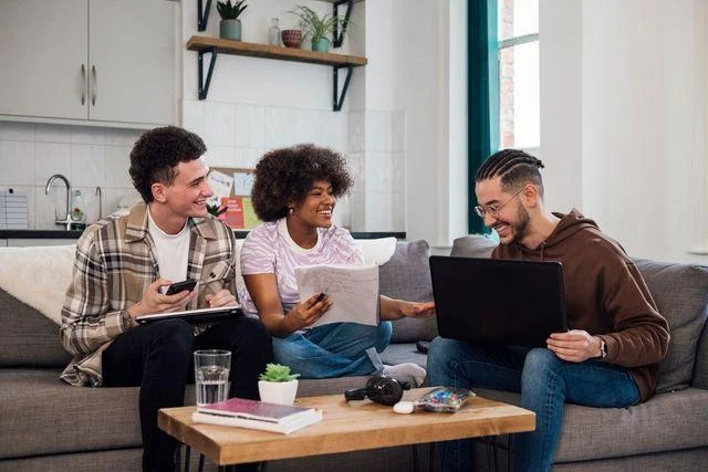 Three roommates laughing together while reviewing documents in a shared apartment