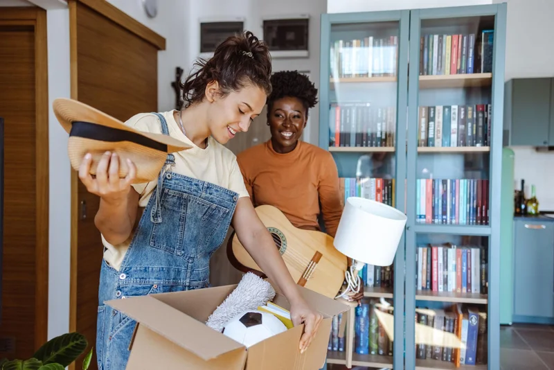 Friends smiling while unpacking books in their new apartment