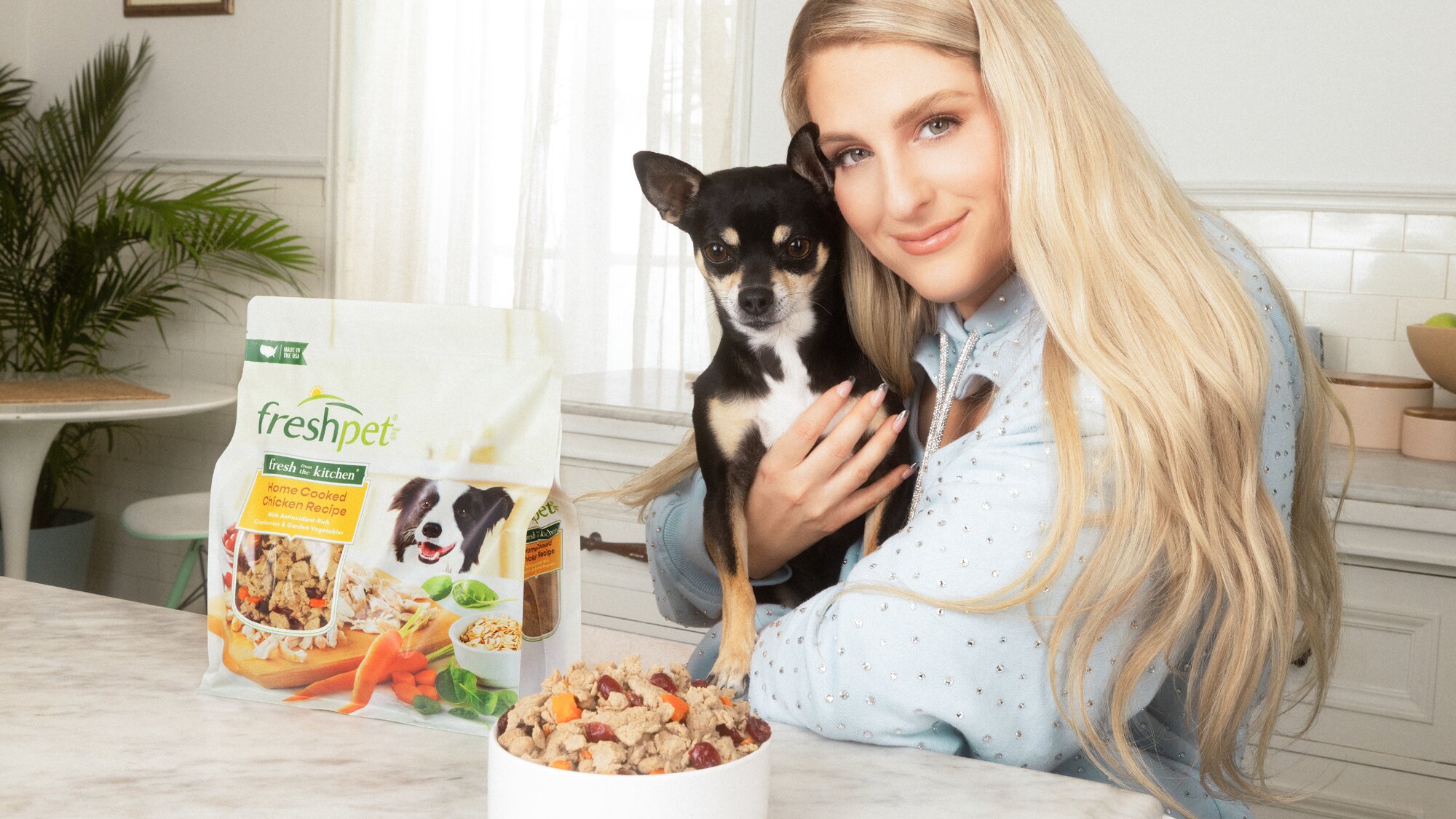 Meghan Trainor holding a dog with a bag of Freshpet on a table.
