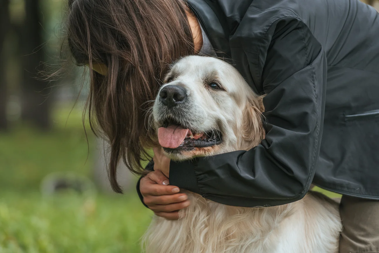 A pet parent hugging their dog ourdoors.