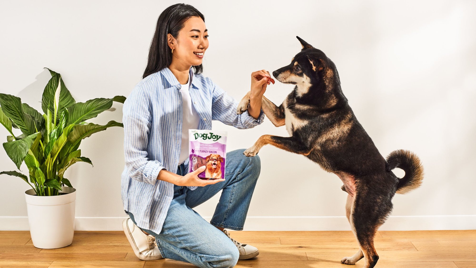 A woman kneeling down to give her dog a Dog Joy treat. 