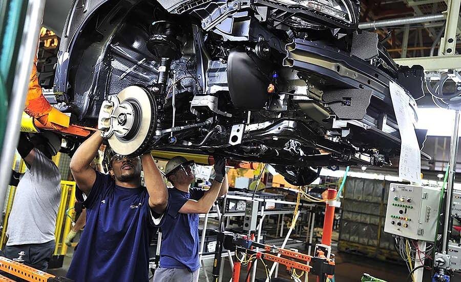 Workers installing parts on the underside of a vehicle on the Subaru assembly line