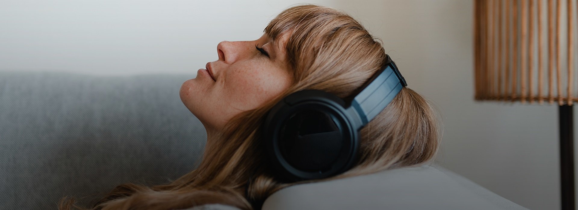 A woman is lying on the couch and listening to music on headphones
