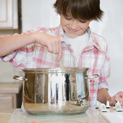 Boy stirring a pot on top of a stove.