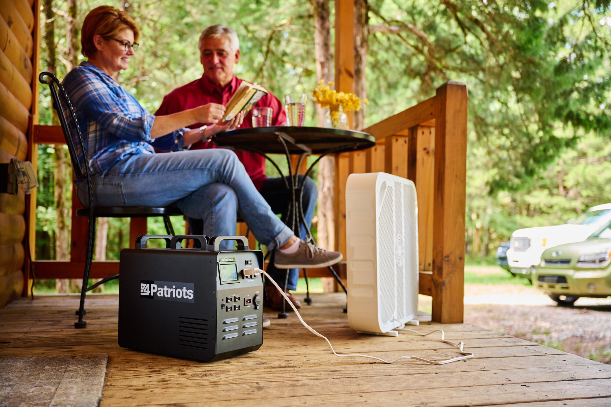 A husband and wife sitting on their front porch with a box fan plugged into their Patriot Power Generator to keep them cool on a hot day